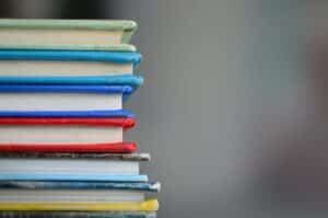 A stack of books with different colour covers - yellow, blue, red, blue, blue, green.