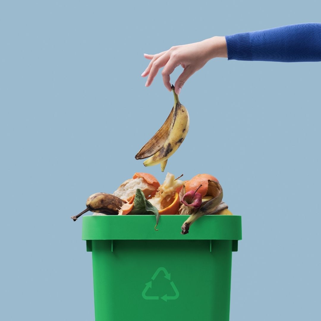 Green food waste caddy filled with fruit peels. Woman adding a banana skin to the pile - Why kids are recycling superheroes