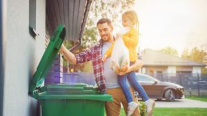 a father holding his young daughter encouraging her to recycle